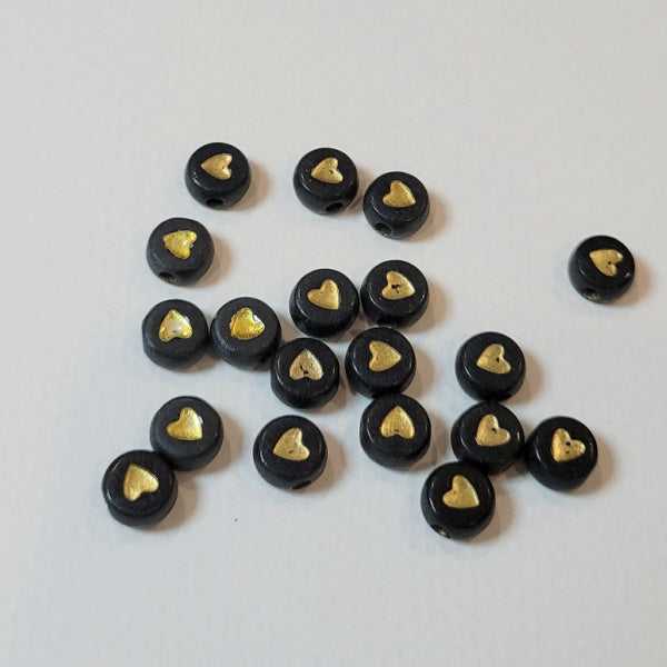 A collection of black round acrylic beads with gold metallic hearts, intended for crafting jewelry such as bracelets.